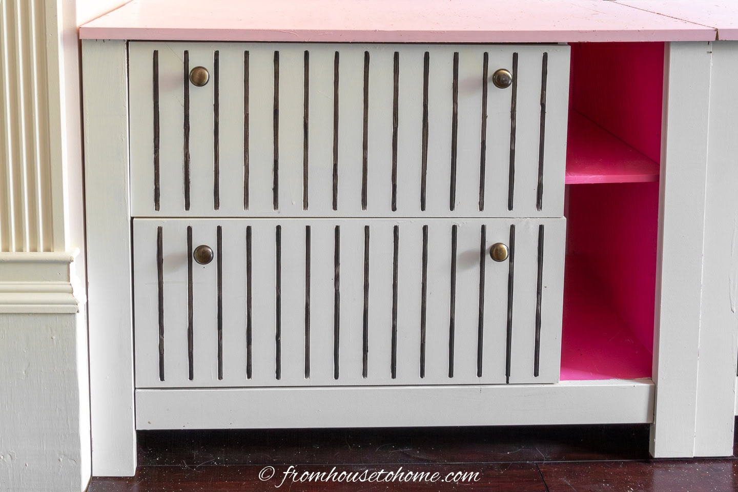 close up of a filing cabinet painted white with a light pink top, bright pink insides, and black pin stripes on the drawers