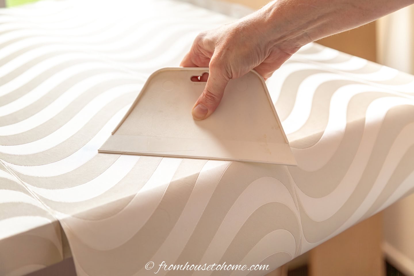 A wallpaper smoother being used to smooth bubbles out of wallpaper on a countertop