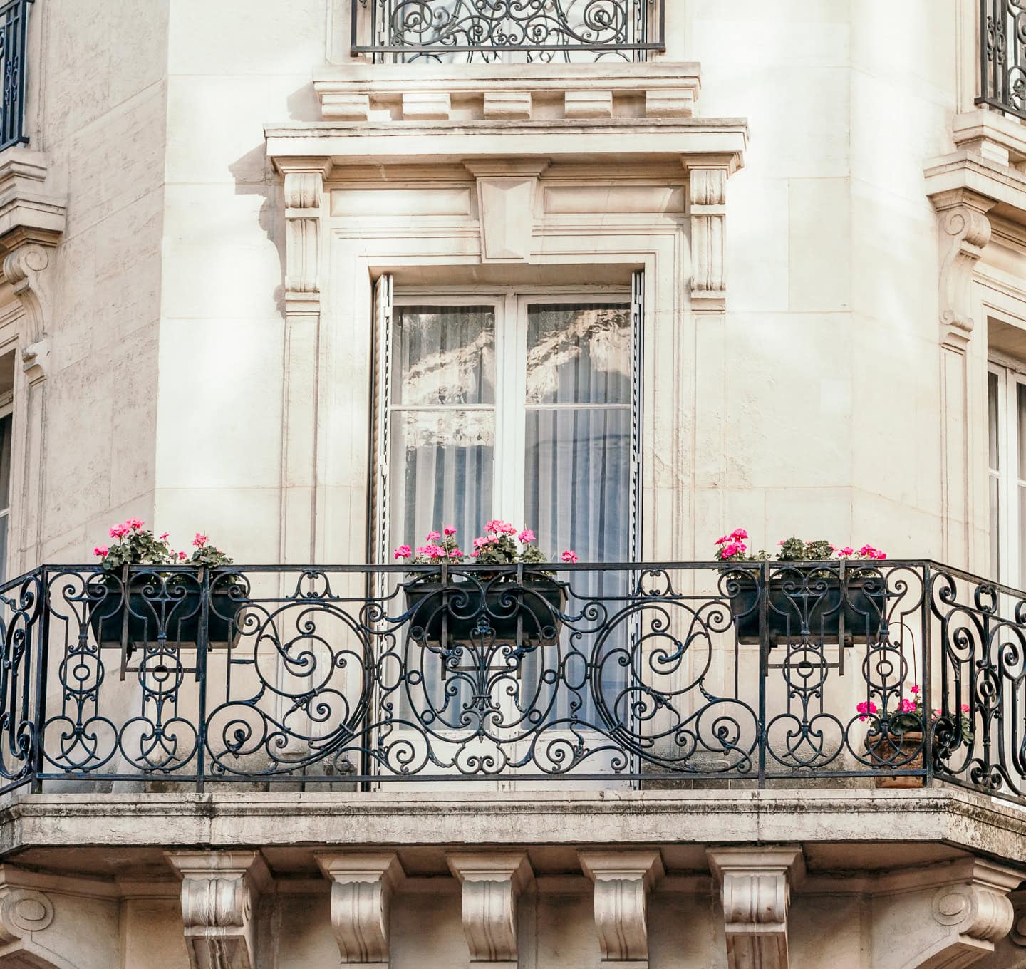 The outside of a white Paris apartment building with wrought iron railings and pink flowers.