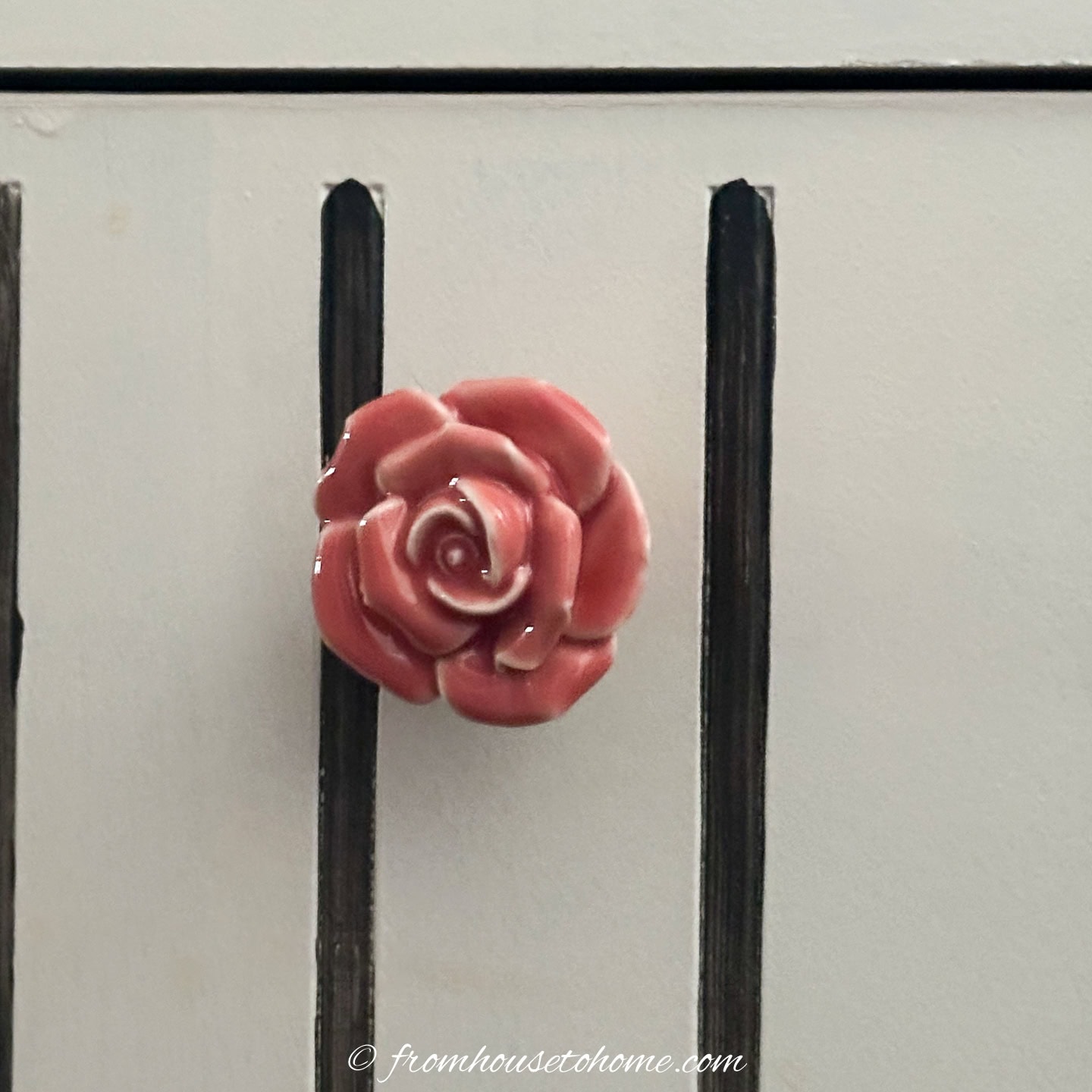 A close up of a ceramic pink rose knob on a black and white filing cabinet