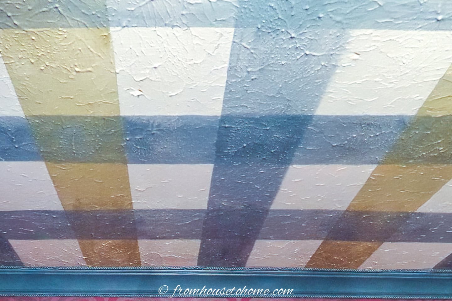 blue and yellow stripes painted perpendicular to blue stripes on an ivory ceiling