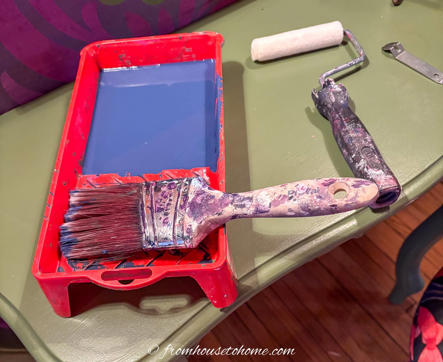 Small paint tray filled with navy blue paint, a brush and a small wool roller