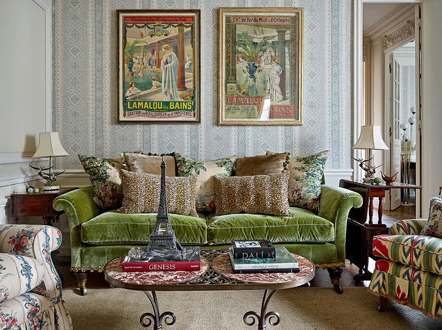 A living room with a green velvet sofa, patterned pillows, framed posters on the wall, and a coffee table with books and a decorative Eiffel Tower.
