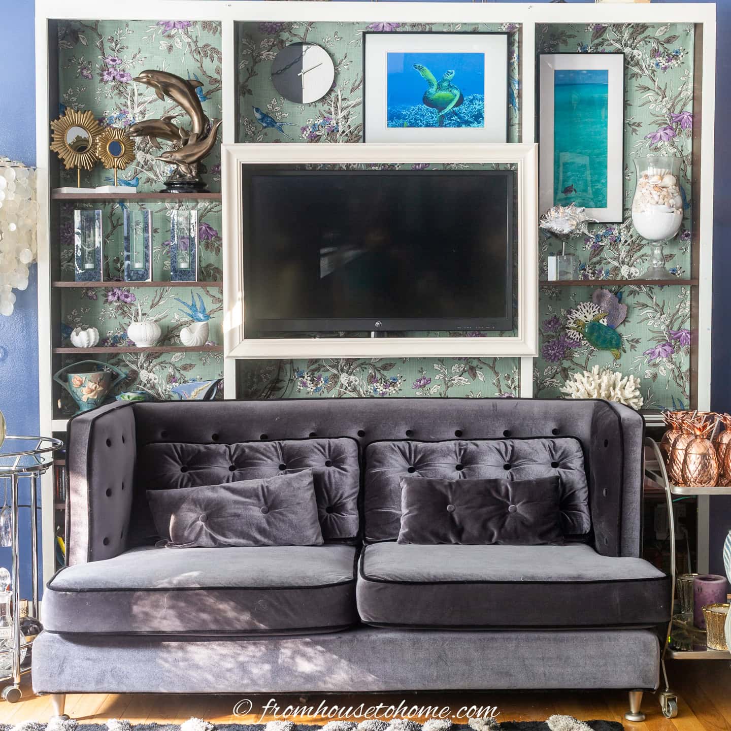 A grey velvet sofa with a bookshelf behind it