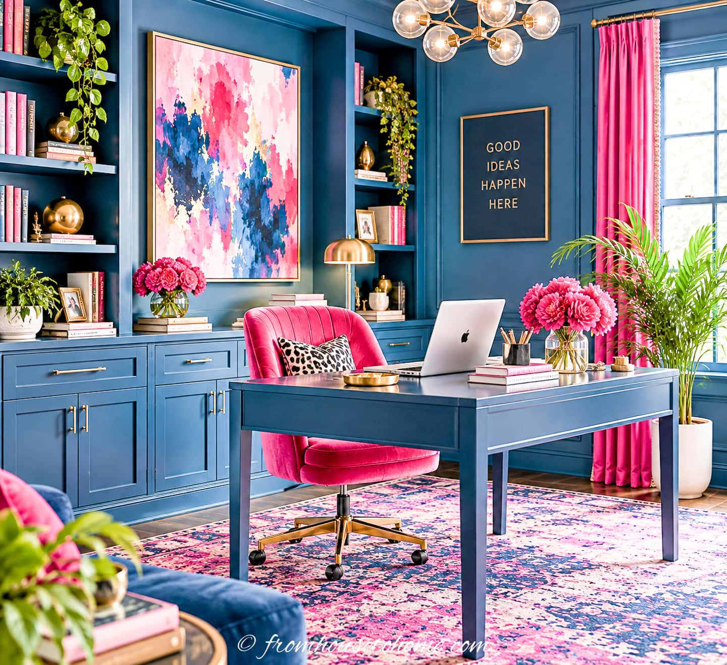 A blue office with a pops of fuchsia in the chair, curtains, artwork and rug