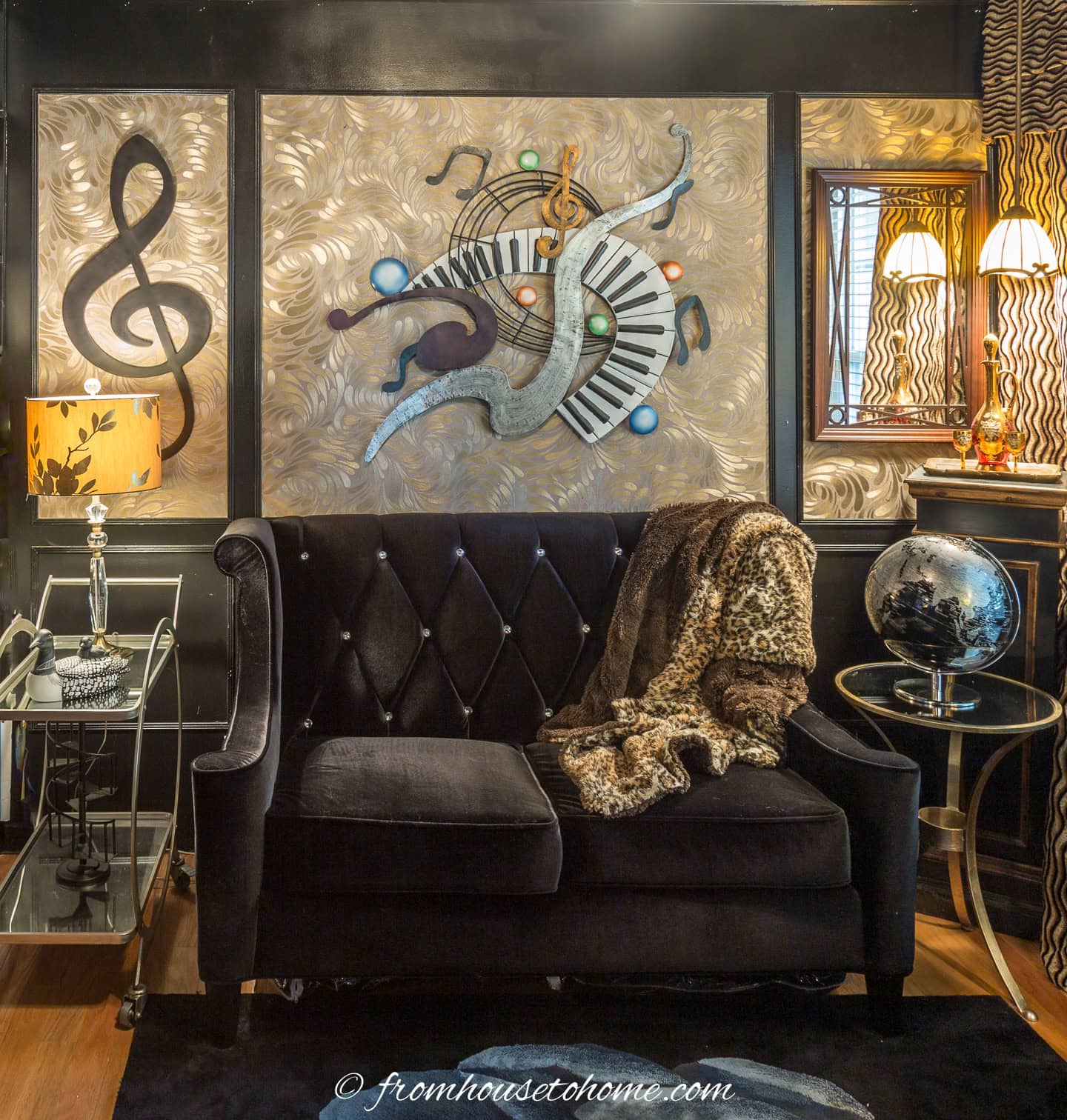A living room wall with gold wallpaper inside of picture molding on a black wall behind a black sofa