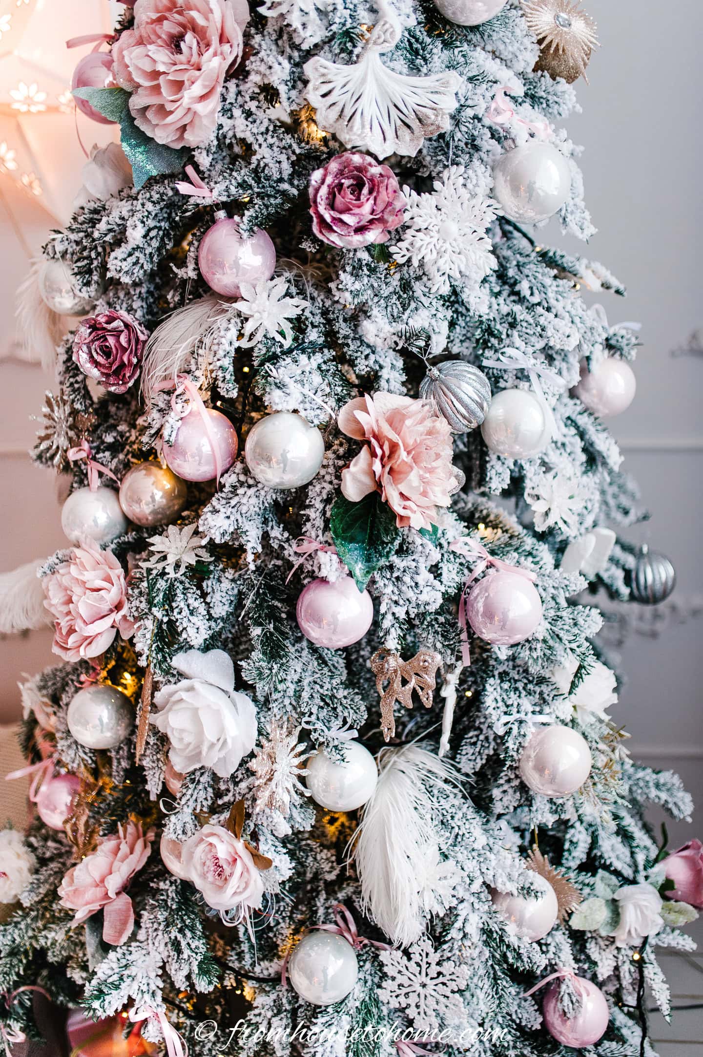 A Christmas tree decorated with pink flowers, pink and white ornaments and feathers