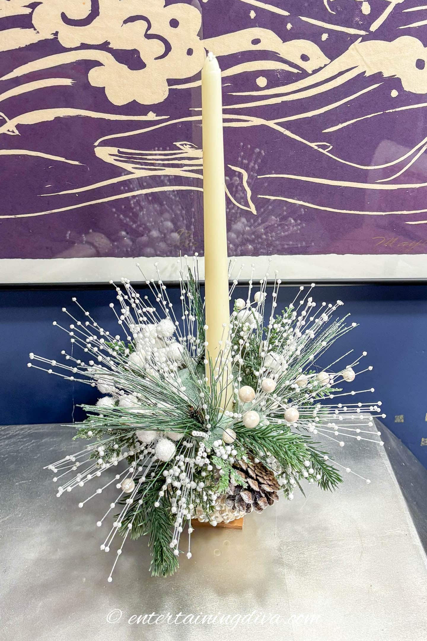 A small DIY Christmas ornament centerpiece with a white candle on a table