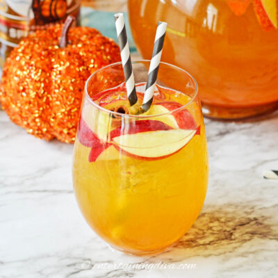 close up of a glass of pumpkin sangria garnished with apple slices, a cinnamon stick and two straws