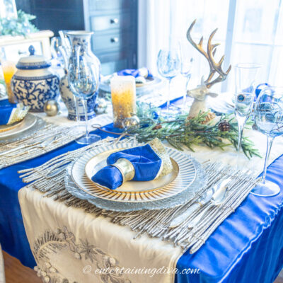 Blue, white and gold Christmas tablescape with a blue tablecloth, white runners and a blue, white and gold place setting