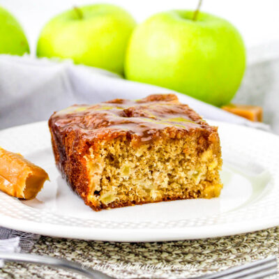 close up of a piece of caramel apple sheet cake on a plate in front of green apples